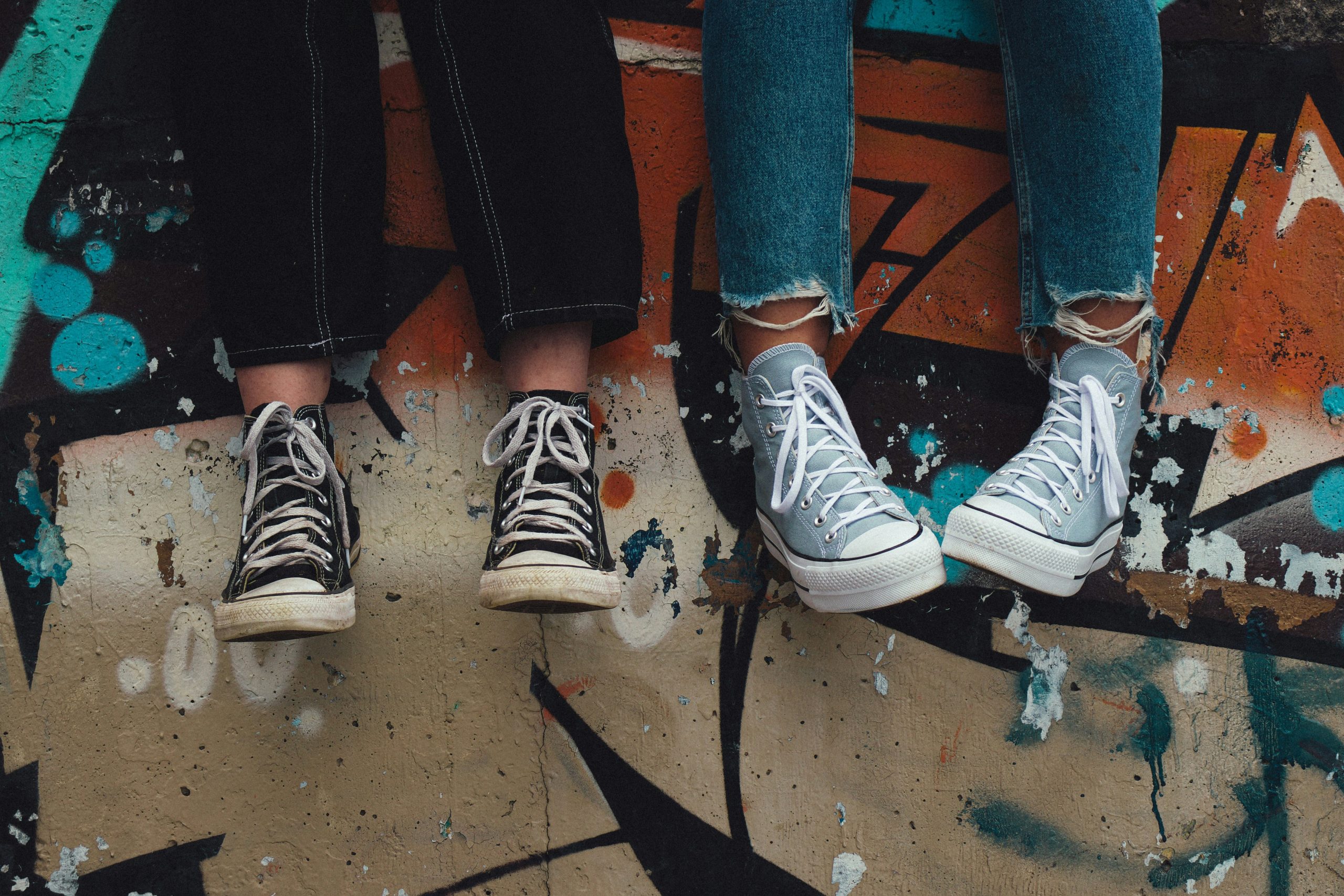 Adolescence and Hot Chicks - image of 2 sets of legs in jeans and converse sneakers against a graffiti wall