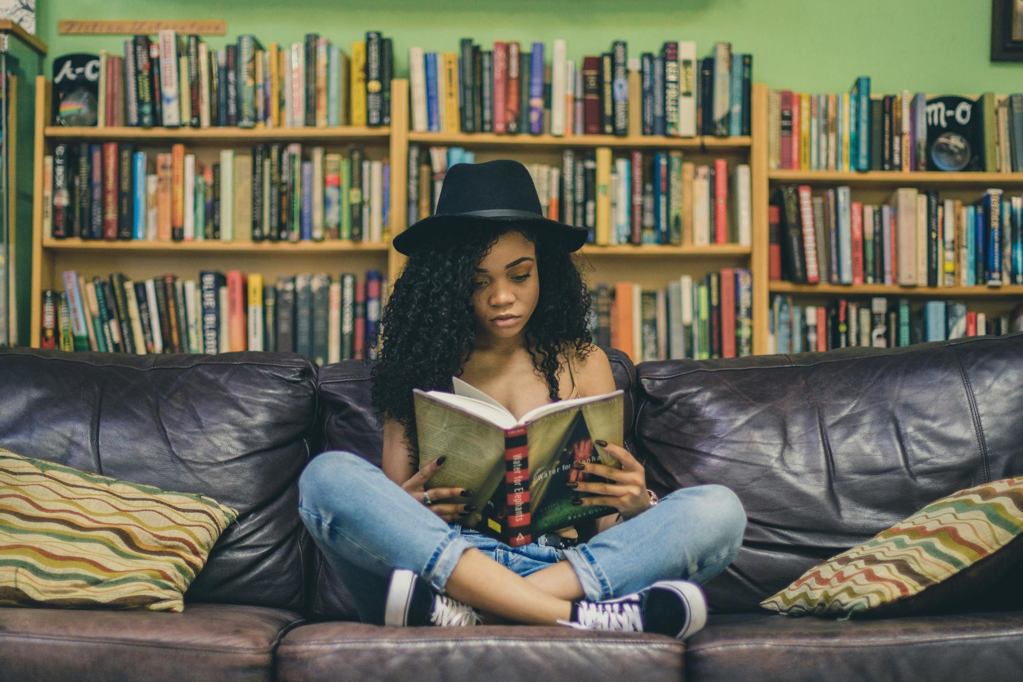 Image of a woman sitting cross-legged on a leather sofa reading for pleasure